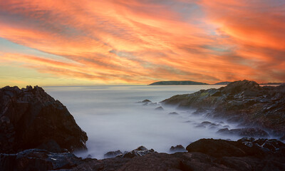 Landscape view of colorful evening sunset reflection over rocky coastal headland. Coffs Harbour, Australia.