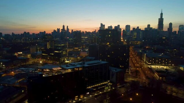 A captivating drone aerial view panning right of Chicago at dusk showcasing illuminated skyscrapers against the darkening sky The golden hues of sunset paint are highlighting architectural marvels