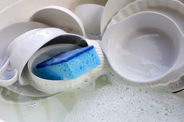 Dirty dishes with cleaning sponge in foam of dishwashing liquid. Washing dishes concept