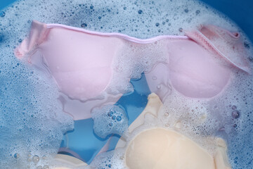 Lady bra soaked in water dissolved detergent with white foam bubble. Laundry concept