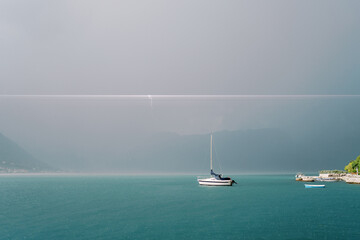 Sailing yacht sails on the sea against the backdrop of a thunderstorm front in the mountains
