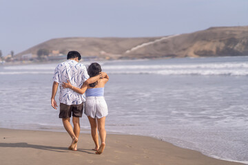 Fototapeta na wymiar Couple in love walking hugging each other along the seashore