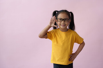 A little Asian girl holds her hands close to her ears and pretends to listen to the excited face of...