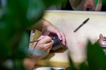 A traditional craftsman is carving and making a Chinese purple sand tea cup