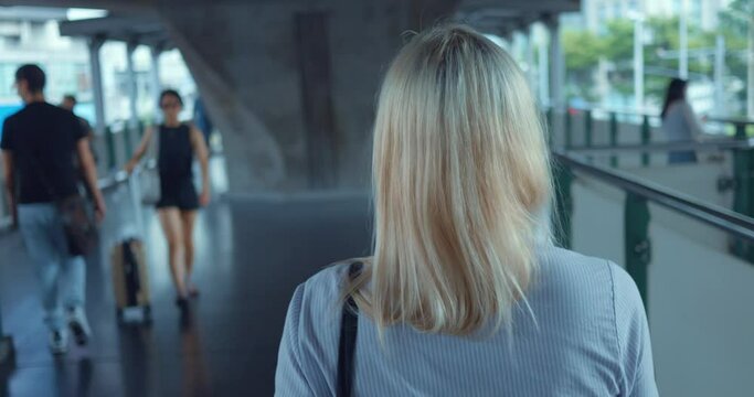 Woman walking strolling through city. Back tracking shot. Back view of unrecognizable woman walks along city center bridge looks around busy city on background business downtown. Close up, tracking