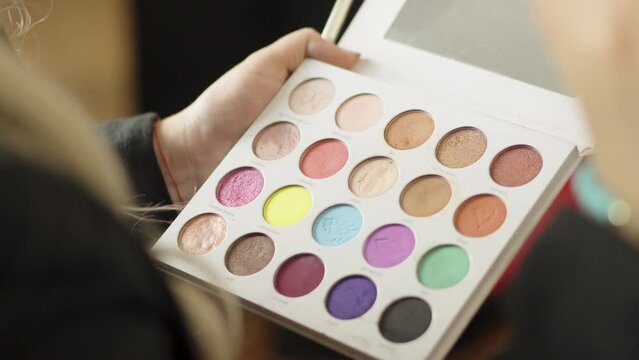 A professional makeup artist works with an eyeshadow palette of various colors