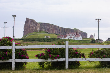 vue sur un terrain avec du gazon vert protégé par une clôture blanche en bois avec une falaise en arrière plan lors d'une journée d'été grise