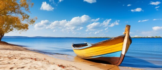 Fototapeta premium A sunny day at the beach with a small wooden boat resting on the sand, framed by a lush green tree in the background