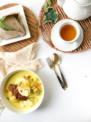 A bowl of “Lontong” or rice cake and coconut gravy with tumeric, chilli, and vegetables with some shadow and selective focus.