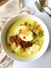 A bowl of “Lontong” or rice cake and coconut gravy with tumeric, chilli, and vegetables with some shadow and selective focus.