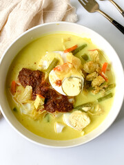 A bowl of “Lontong” or rice cake and coconut gravy with tumeric, chilli, and vegetables with some shadow and selective focus.