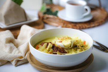 A bowl of “Lontong” or rice cake and coconut gravy with tumeric, chilli, and vegetables with some shadow and selective focus.