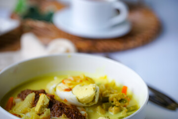 A bowl of “Lontong” or rice cake and coconut gravy with tumeric, chilli, and vegetables with some shadow and selective focus.