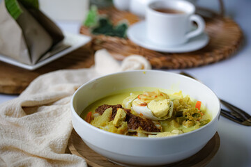 A bowl of “Lontong” or rice cake and coconut gravy with tumeric, chilli, and vegetables with some shadow and selective focus.