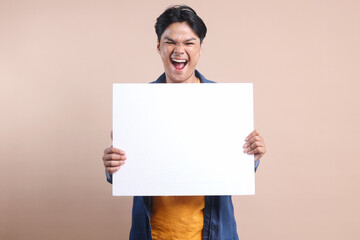 Excited young man holding white blank board for text or ads with happy expression