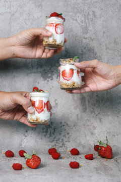 People hands holding strawberry parfait in a glass over grey background