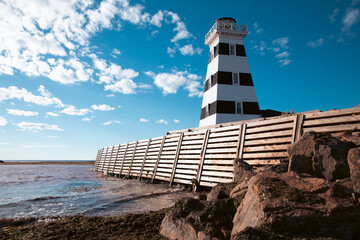 vue en bas angle sur un phare ligné noir et blanc en bord de mer avec un brise-vague en bois et des roches en avant plan