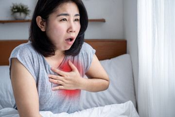 Coronary artery disease CAD concept with asian woman suffering from chest pain, shortness of breath and heart attack in bed