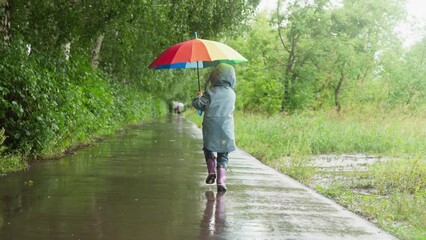 Kid runs in park with colorful umbrella. Child carefree spirit shines brightly among gray surroundings. Joy and freedom in dreary rainy day
