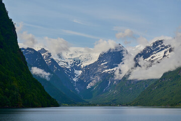 tranquil and calm Oldevatnet glacial lake in front of the melting Briksdalsbren glacier in Norway with snow capped mountains.