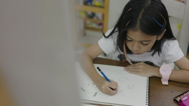 A young girl is drawing a picture of a bird on a piece of paper. She is using a blue pencil and is sitting at a desk
