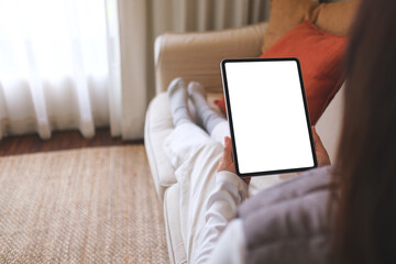 Mockup image of a woman holding digital tablet with blank desktop screen while sitting on a sofa at home - obrazy, fototapety, plakaty