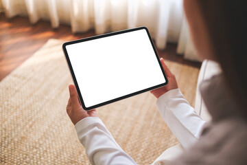 Mockup image of a woman holding digital tablet with blank desktop screen while sitting on a sofa at...