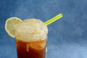 cola with ice and lemon with foam spilling out of the crystal glass