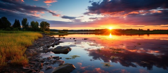 Tranquil sunset scene over a calm lake, highlighted by rocks and grass in the foreground