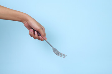 Woman's hand holds a metal fork on a blue background.