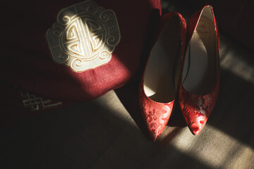 A pair of elegant red floral high-heeled shoes beside an embroidered cushion, bathed in warm...