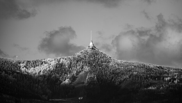 A crisp morning view of the snow-covered Jested peak with its iconic tower standing tall against a blue sky. Liberec, Czechia. Black and white image.