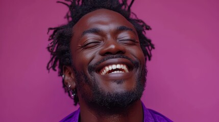   A man with dreadlocks wears a smiling expression as he gazes at the camera, donning a purple shirt and earrings