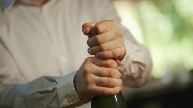 A man removes the cork and opens a bottle of champagne to celebrate. Close up and slow motion