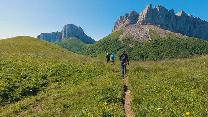 A group of hikers make their way along a narrow trail amidst lush greenery, heading for a rocky...