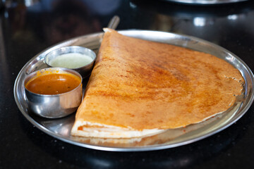 A delicious, crispy dosa served with savory sambar and coconut chutney on a stainless steel plate, capturing the essence of South Indian cuisine.