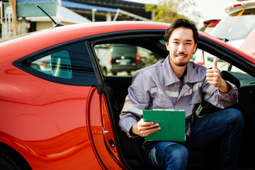A Japanese export auto mechanic man give a thumb up, holding note pad to check up inside the car for fixing and repair. Asian auto car repair shop service center. Outdoor professional service. - 774658518