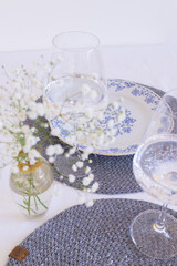 Elegant table setting with wineglass, plate and small glass vase with gypsophila wicker gray table-napkin. Stylish decor