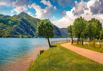 Sunny morning view of Idro lake with green tree and tourist pathway. Colorful  summer scene of Anfo...