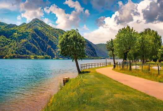 Sunny morning view of Idro lake with green tree and tourist pathway. Colorful  summer scene of Anfo comune in the province of Brescia in northern Italy, Europe. Beauty of nature concept background.
