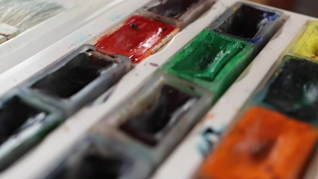 Set of multicolored watercolor paints and white ceramic palette close up in art studio. Artist's tools and colors on horizontal video