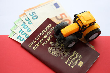 Red polish passport and yellow tractor on euro money and smooth red and white flag of Poland close up - obrazy, fototapety, plakaty