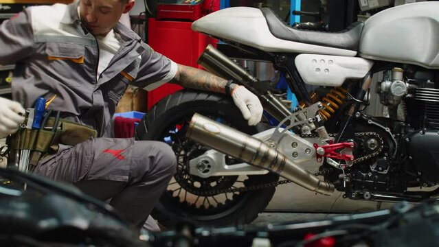 Wide shot of multiethnic repairman inspecting clients motorcycle with tools while working in repairing shop