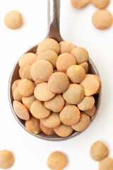 Dry brown lentils in iron spoon on white background. Close-up