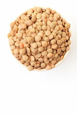 Uncooked brown lentils in bowl on white background. Dry brown lentil grains. Top view. Space for a text