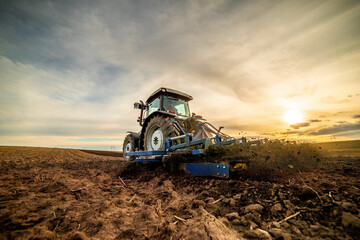 Wide-angle view of a tractor plowing farmland against a dramatic sunset sky