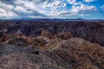 Fototapeta na wymiar Sandy relief canyons carved by water and wind, reminiscent of a lunar and Martian landscape against a background of blue sky with clouds and rich desert vegetation