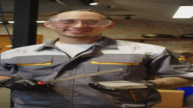 Vertical portrait of multiethnic technician in googles with sharpening stone looking at camera in garage or workshop