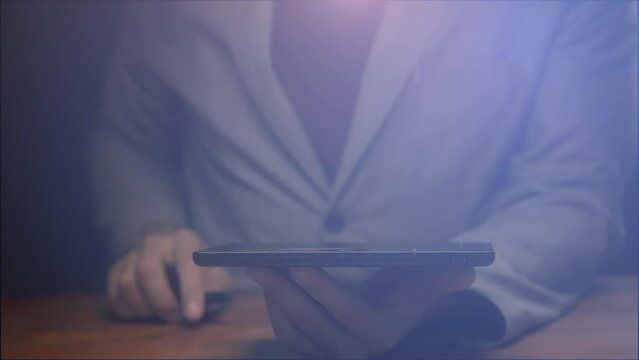 Silhouette of a businessman without a face sitting at a table with an electronic tablet in blur with light correction. Background and basis for footage
