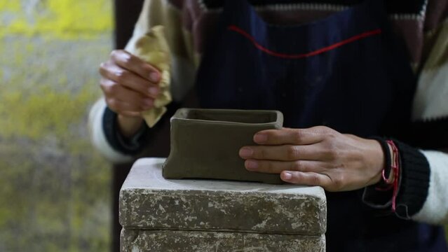 Close up over the hands of a mexican craftswoman moistening the final part of a clay craft